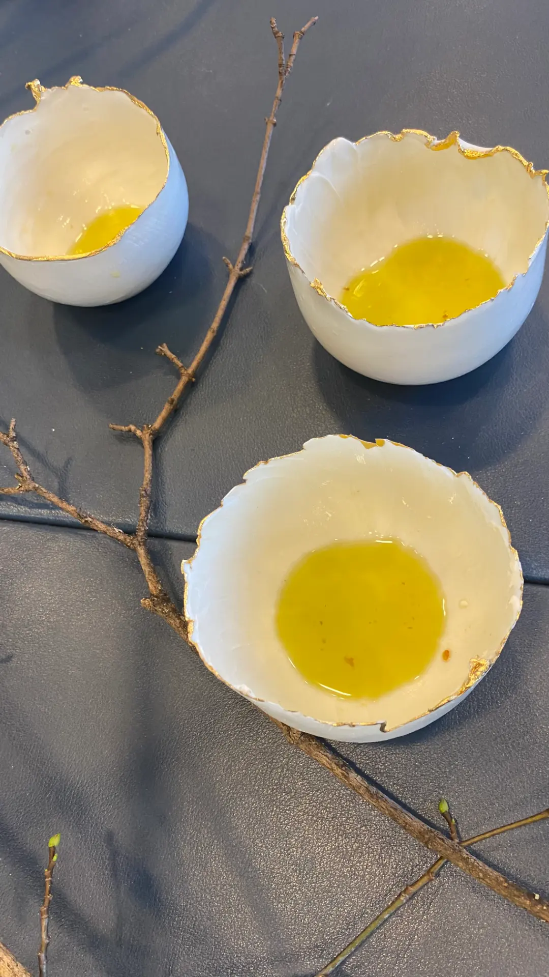 Vagal Foods exhibition table in Vienna: three porcelain bowls with gilded rims holding olive oil, arranged around a bare branch