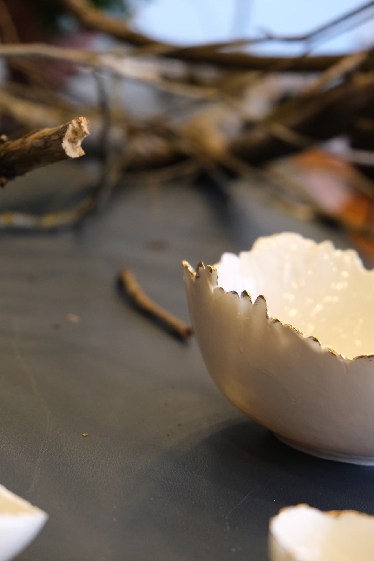 A close porcelain bowl with a serrated gilded rim, photographed against the soft grey of the table