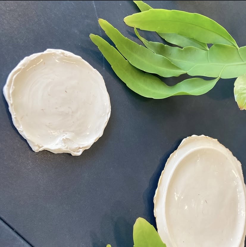Two porcelain dishes with soft, torn edges beside green leaves, by Atelier VOTE.